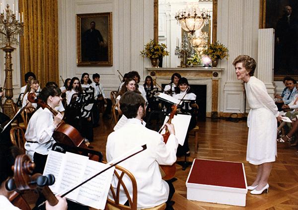 woman in white dress speaks to orchestra